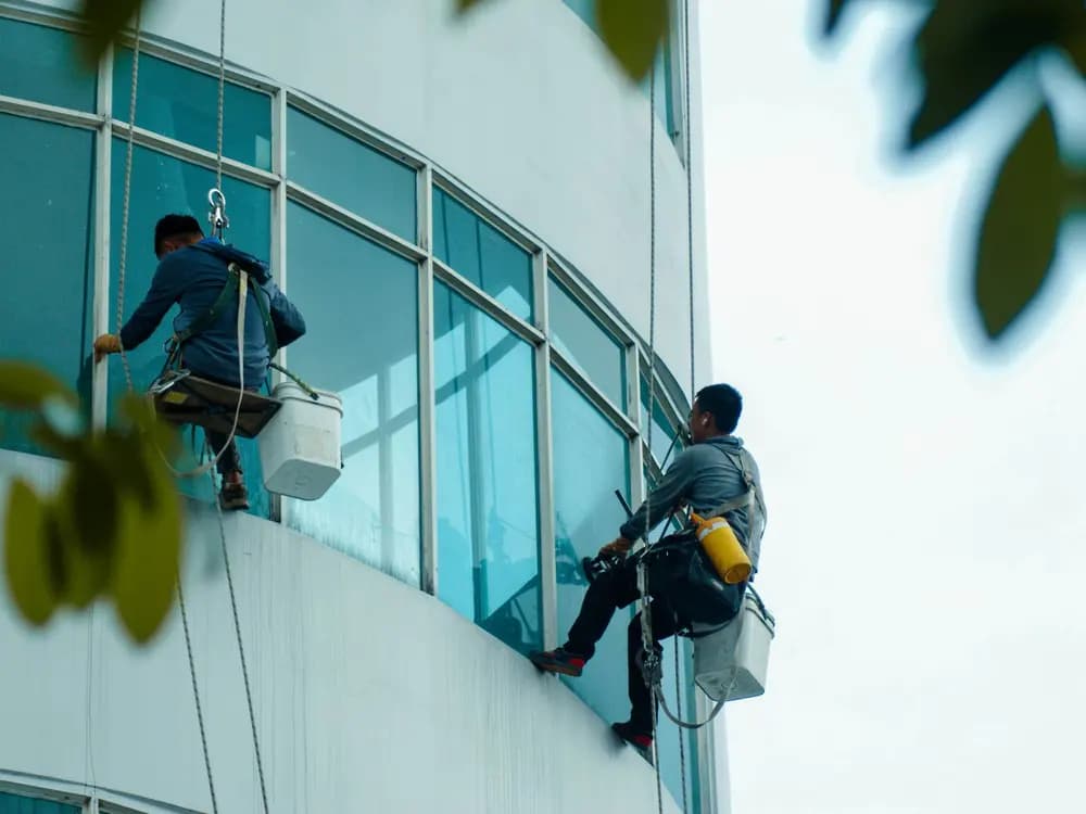 Técnicos sellando juntas en una fachada de cristal y aluminio con acceso por cuerda